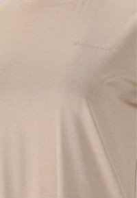 Beige sport t-shirt i lätt material. Har rund hals och subtil textur. Ordet "ENDURANCE" är präglat på framsidan.