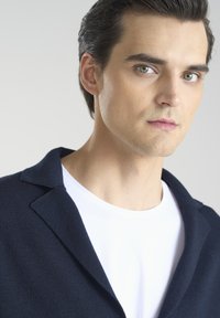 Granatowa marynarka o fakturze noszona na białej koszuli, z dopasowanym kołnierzykiem i czystymi liniami, podkreślająca prosty, nowoczesny design.