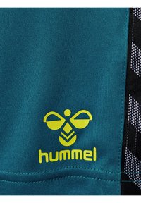 Gult Hummel-logo med en stiliserad bi och text på en tealfärgad tygbakgrund med svartvitt geometriskt mönster på sidan.
