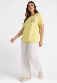 Camiseta amarilla de manga corta para mujer con gráfico de "NEW YORK", combinada con pantalones anchos blancos y zapatillas ligeras.