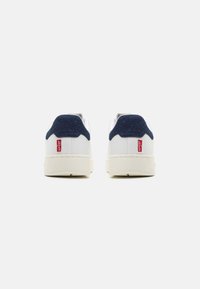 Sneakers bianchi con un accento in pelle texturizzata blu navy sul tallone. Presentano una suola in gomma e un'etichetta rossa sul retro. Parte superiore in pelle liscia.