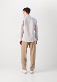 Striped long-sleeve shirt in light shades, tailored fit, with a button-down collar; paired with beige pants and white sneakers.