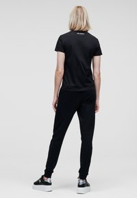 Svart bomulls t-shirt med korta ärmar, ihop med svarta joggers med sidodetaljer. Modellen bär svarta sneakers med tjocka vita sulor.