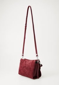 Red suede crossbody bag with a textured strap and silver hardware, featuring a soft, structured shape and a spacious interior.