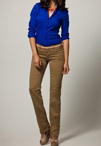 Kunglig blå långärmad skjorta med knappar kombinerad med tanfärgade, figurnära byxor och beige kilklackskor. Framträdande halsbanddetalj.