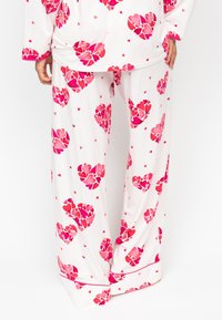 Witte pyjamabroek met grote roze en rode hartpatronen, gemaakt van zachte stof, met een relaxed fit en omgeslagen zoomdetails.