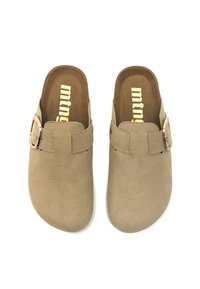 Zuecos beige sin cierre con un upper de textura similar a la gamuza, que cuentan con una correa lateral y una hebilla de metal. Plantillas interiores de color marrón suave con el logo de la marca.