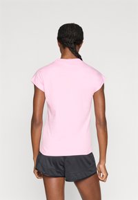 Ružové tričko s krátkym rukávom a okrúhlym výstrihom, vyrobené z jemnej látky. Nosené s čiernymi športovými šortkami. Čisté línie, jednoduchý dizajn.