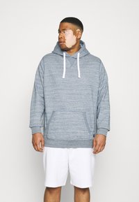 Felpa grigia con texture e tasca a marsupio, con lacci bianchi e polsini a costine, abbinata a pantaloni corti bianchi. Design semplice e casual.