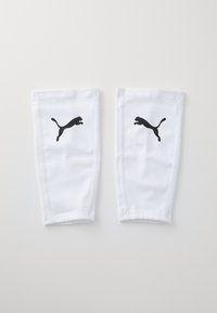 Bílé sportovní návleky na nohy vyrobené z hladké tkaniny, s černým logem Puma na přední straně a zesíleným švem na okrajích.