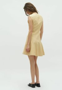 Abito giallo senza maniche con gonna a ruota, realizzato in tessuto morbido, caratterizzato da un design pulito e dettagli di cucitura minimi.