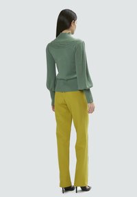 Maglione verde a maglia con collo alto e maniche a sbuffo, abbinato a pantaloni gialli a vita alta, indossati con tacchi neri.