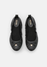 Paire de ballerines en cuir noir Michael Kors avec bouts arrondis, petits nœuds et breloques carrées dorées sur fond blanc.