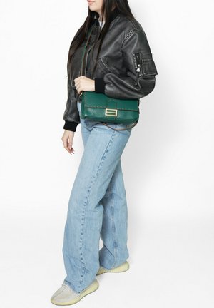 Zwarte leren bomberjack met geribbelde mouwen, lichtblauwe wijde jeans en een groene gestructureerde schoudertas met goudkleurige hardware.