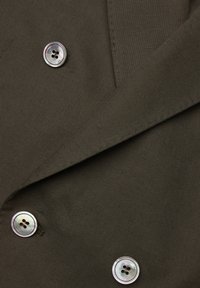 Olivgrönt tyg, texturerat och mjukt, med dubbelknäppt design, silverknappar och spetsiga slag.