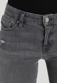 Jeans de mezclilla gris de tiro alto con textura deslavada, ligero desgaste, un bolsillo frontal y cierre de botón plateado.