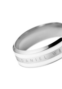 Hopeakääty, jossa on kolme raitaa; kaksi kiiltävää hopeaa ja yksi mattavalkoinen. Kaiverrettu teksti "DANIEL WELLINGTON" renkaan ympäri.