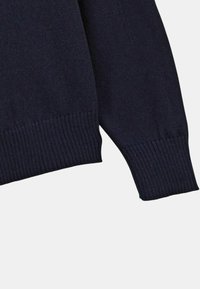 Manche et partie inférieure d'un pull en maille bleu marine foncé avec des poignets et un ourlet côtelés sur fond clair.