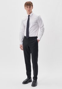 White long-sleeve dress shirt paired with black tapered trousers and black loafers. The shirt features a classic collar and buttoned cuffs.
