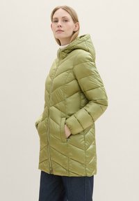 Giacca a vento verde con cappuccio, caratterizzata da un motivo a zigzag, chiusura con zip e tasche laterali, realizzata in tessuto lucido e leggero.
