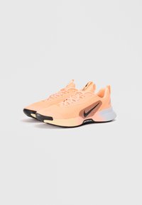 Chaussures de sport Nike en mesh pêche clair avec logo en accent noir, offrant une semelle rembourrée, un design à lacets et des superpositions texturées.