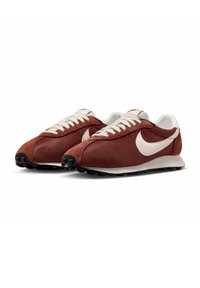 Ténis de tecido vermelho com logo Swoosh branco, apresentando um upper texturizado, fecho com atacadores tradicional e sola de borracha preta.