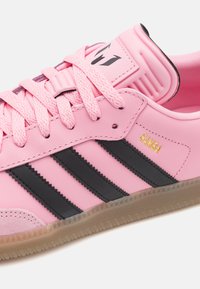 Pink leather sneaker with black stripes, featuring a textured sole, rounded toe, and logo on tongue. Lace-up closure with matching laces.