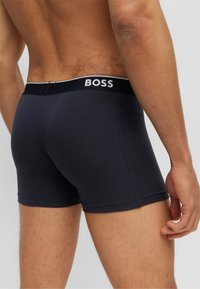 Tumed sinised boxershorts pehmest kangast, musta vööga, millel on valge tekst "BOSS". Sile tekstuur ja liikuv disain.