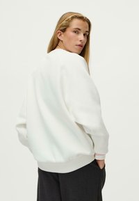 Bela sweatshirt z udobnim krojem, z ribbed manšetami in robom, gladko teksturo in krojaškim izrezom, v kombinaciji s temnimi hlačami.