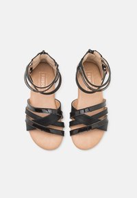 Mustat patentti-nahkasaappaat, joissa on useita ristikkäisiä hihnoja. Litteät pohjat ja nilkkahihnat. Beige sisävuori. Yksinkertainen ja avoin muotoilu.