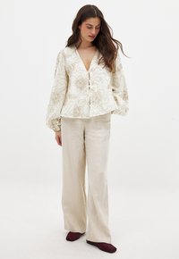 White floral-patterned blouse with a deep V-neck, balloon sleeves, and tie front detail, paired with light beige wide-leg pants.