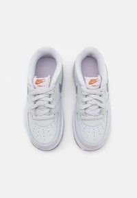 Ett par vita Nike Force 1-sneakers med orange loggor, snören knutna, sedd uppifrån på en vit bakgrund.