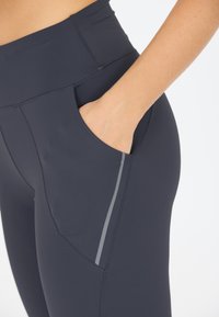 Leggings sportivi blu navy con vita alta, tasca laterale e una striscia riflettente lungo la cucitura della tasca. Tessuto liscia e elasticizzato.