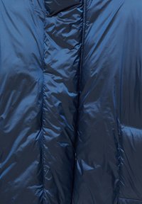 Kurtka puchowa w ciemnym niebieskim kolorze, o błyszczącej, pikowanej teksturze, z przednim zamkiem błyskawicznym, wysokim kołnierzem i boczną kieszenią.