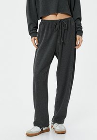 Grijze, gestructureerde broek met elastische taille en een trekkoord. Losse pasvorm, taps toelopende benen, gecombineerd met witte sneakers en een cropped sweatshirt.