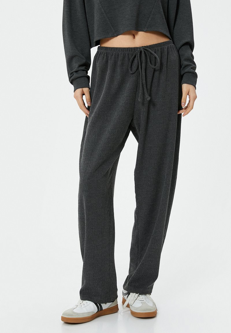 Grijze, gestructureerde broek met elastische taille en een trekkoord. Losse pasvorm, taps toelopende benen, gecombineerd met witte sneakers en een cropped sweatshirt.