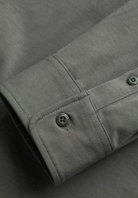 Grauer Baumwollhemdärmel mit Knopfverschluss, subtiler Textur und kontrastierendem Stich für Haltbarkeit und Detailreichtum.
