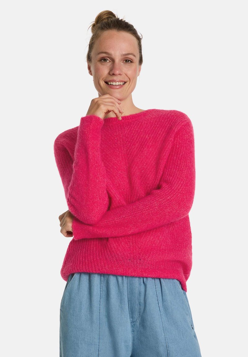 Helles pinkes Sweatshirt aus strukturiertem Strick, mit rundem Halsausschnitt und langen Ärmeln, kombiniert mit blauen, locker sitzenden Hosen.