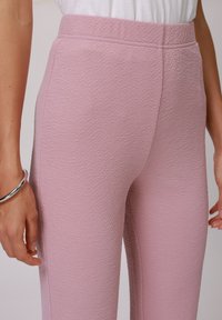 Roze teksturirane hlače s prilagođenim krojem i glatkim pojasom. Tkanina s blagim reljefnim uzorkom ističe elegantnu siluetu.