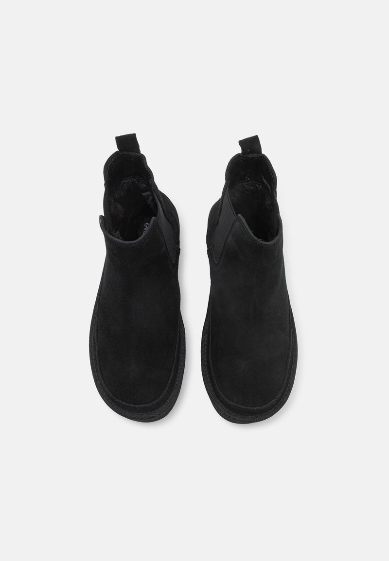 Bottines Chelsea en daim noir avec des panneaux latéraux élastiques et des languettes en tissu. Embout rond et semelle texturée pour améliorer l'adhérence et la durabilité.