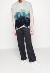 Kortärmad skjorta med en gradientdesign som går från ljus till mörkblå, med spetsig krage, matchad med mörkgrå byxor och vita sneakers.