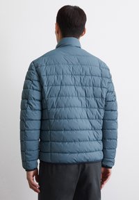 Padded jacket in blue-gray with horizontal stitching, high collar, and long sleeves. Smooth texture with elastic cuffs and hem.