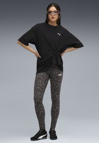 T-shirt nero oversize annodato in vita, abbinato a leggings aderenti con stampa leopardata scura. Sneakers nere completano l'outfit.