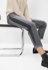 Graue Jeans aus Denim mit einem zweifarbigen Design, das ein dunkleres Seitenpanel, einen schlanken Schnitt und umgeschlagene Säume aufweist. Kombiniert mit einem hellen Pullover und Schuhen.