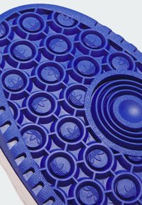 Modrá podrážka topánky s kruhovými a hexagonálnymi vzorami dezénu, na ktorých sú vyrazené logá Adidas trefoil.