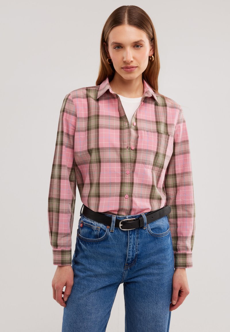 Camicia a quadri rosa e verde con colletto button-down, maniche lunghe e tasca sul petto, abbinata a jeans in denim blu e una cintura nera.