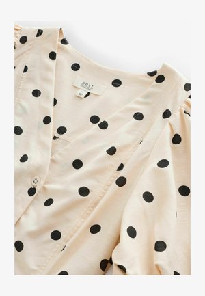 Blouse rose pâle avec des pois noirs, décolleté en V, manches bouffantes et fermeture à boutons. Le tissu comprend du lin pour la texture. Étiquette de marque visible.