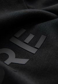 Czarna tkanina o teksturowanej powierzchni z wypukłym, matowym czarnym logo. Logo zawiera geometryczne kształty i linie.