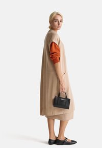 Beige pletené šaty s ribrovou texturou, oranžovými rukávy a černou kabelkou. Mají volný střih a délku po kolena; minimalistický styl.