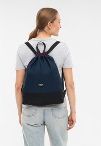 Tengerészeti kék fűzős hátizsák bordó felső részével, fekete aljával és állítható pántjaival. Elöl logó található. Tartós anyag.